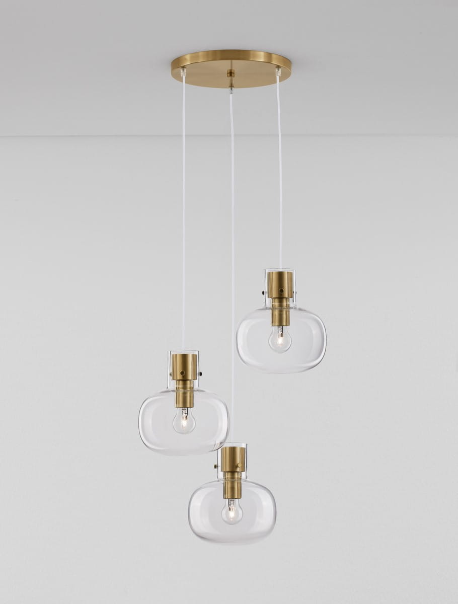 Lampa wisząca Padre z trzema źródłami światła E27, z metalowym złotym mocowaniem i przezroczystymi, szklanymi kloszami o owalnym kształcie. Zawieszona na białych przewodach, umieszczona na prostokątnej podstawie sufitowej.