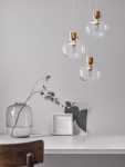 Lampa wisząca Padre z trzema kloszami, wykonana z przezroczystego szkła i złotych detalami. Klosze mają organiczny kształt, zawieszone na białych przewodach. W tle widoczny stół z wazonem, gałązką i ramką na zdjęcia.