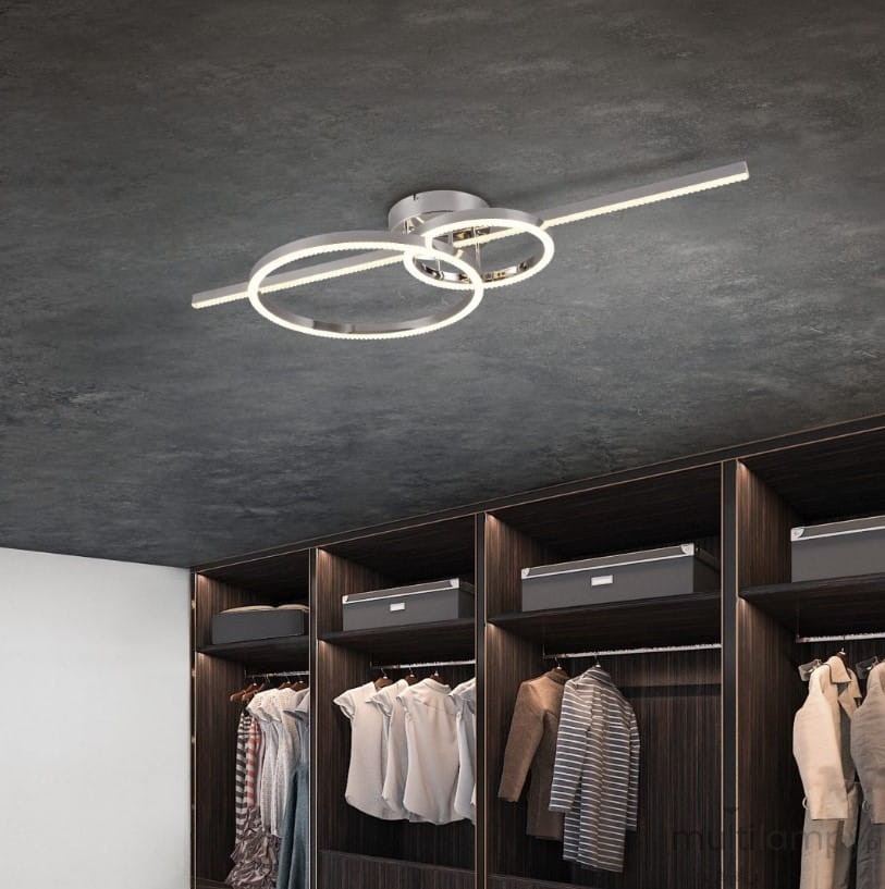 Lampa sufitowa Montilla z pilotem, w kolorze chromu, z trzema źródłami światła LED. Ułożona w nowoczesny sposób, z dwoma okrągłymi pierścieniami, znajdująca się na ciemnym suficie nad szafą z ubraniami.