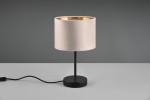 Lampa stołowa Julieta z czarną podstawą i jasnoróżowym kloszem, wykonana z materiału tekstylnego, z wykończeniem w złotym kolorze wewnątrz. Ujęcie z boku, na jasnym stole, widoczny kabel zasilający.