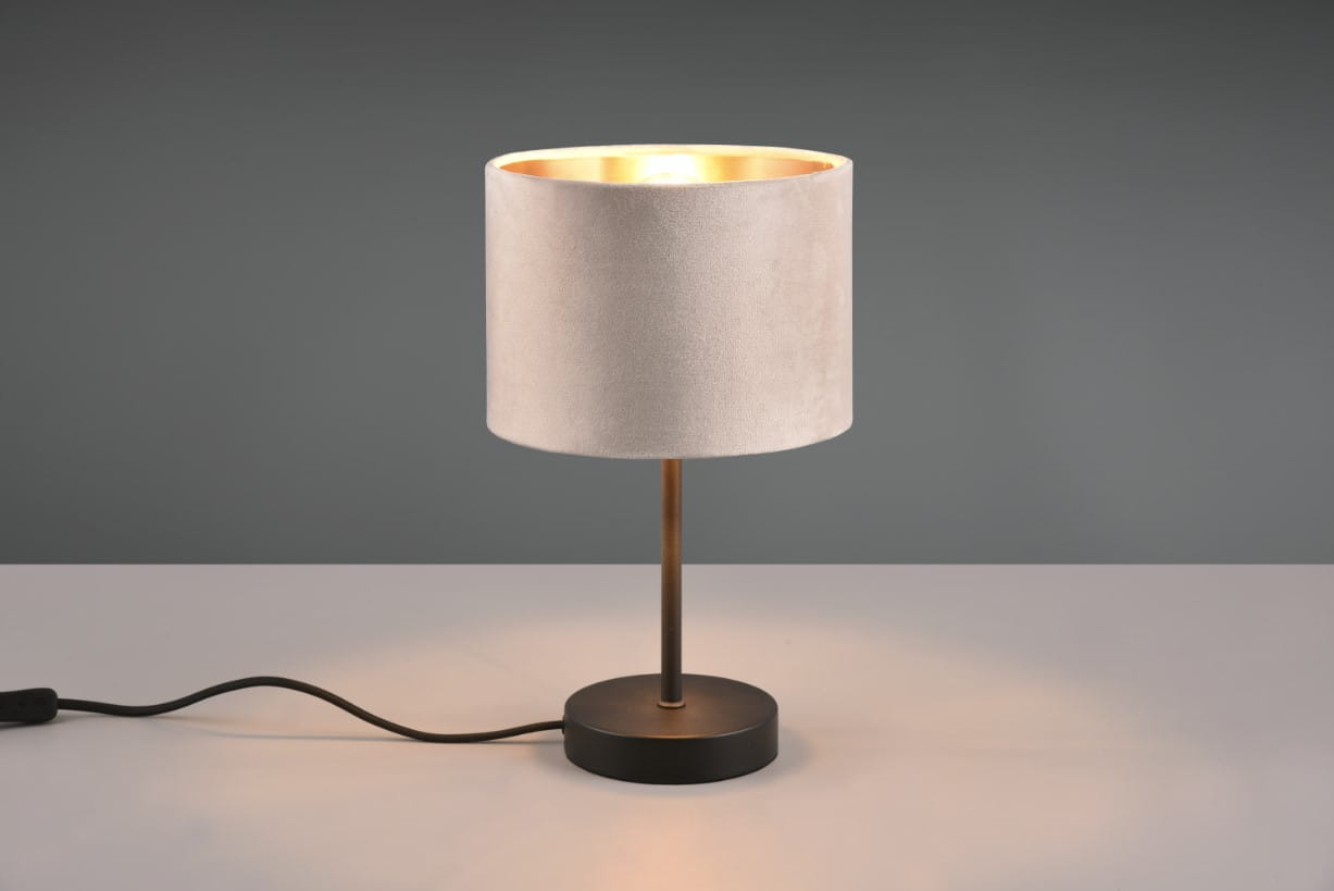 Lampa stołowa Julieta z kloszem w kolorze beżowym i złotym wnętrzem, osadzona na czarnej, okrągłej podstawie. Kabel zasilający widoczny z boku. Ujęcie frontalne, prezentujące całość produktu na jasnym tle.