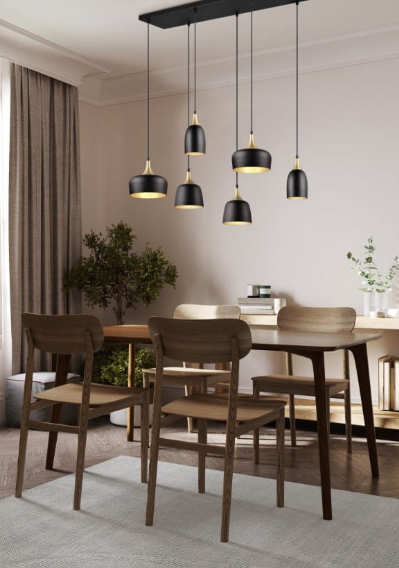 Lampa wisząca Chiraz 6xE27 w kolorze czarnym z elementami złotymi, zawieszona na długich kablach. Widoczna w aranżacji jadalni z drewnianym stołem i krzesłami, w tle roślina oraz zasłony. Kąt ujęcia: frontalny.