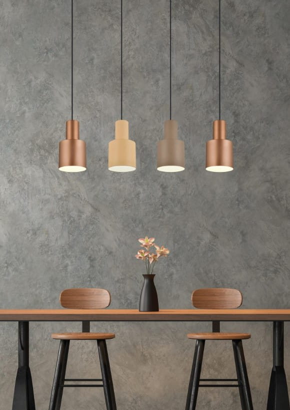 Lampa wisząca Agudo 4xE27 w kolorach miedzi, beżu, szarości i brązu, zawieszona na czarnych kablach. Umieszczona nad drewnianym stołem z dwoma krzesłami, w minimalistycznym wnętrzu z szarym tłem. Wazon z kwiatami na stole.