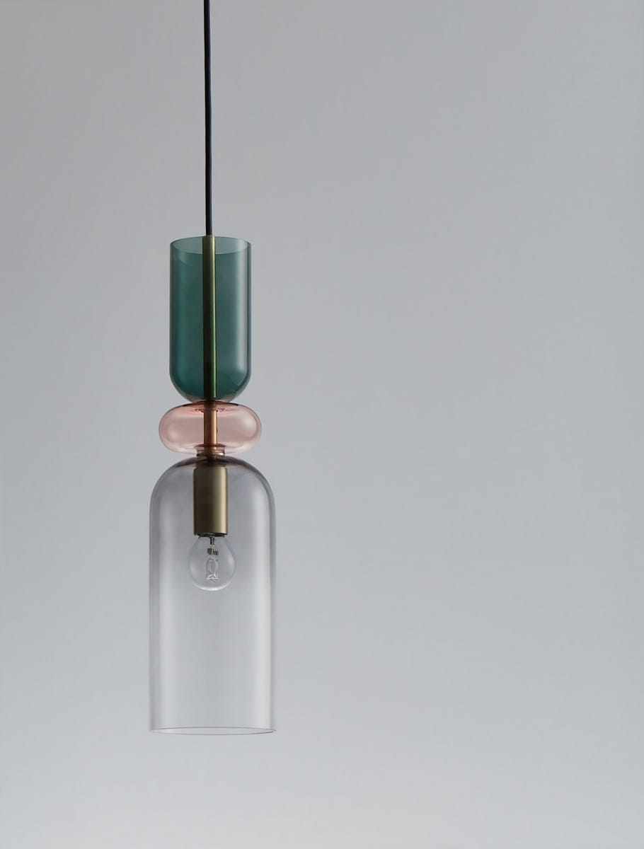 Lampa wisząca Balam 1xE14 w kolorze złotym, z przezroczystym szklanym kloszem w kształcie dzwonu oraz kolorowymi akcentami: zielonym i różowym. Zawieszona na cienkim przewodzie, w prostym, jasnym tle. Idealna do nowoczesnych wnętrz.