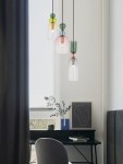 Lampa wisząca Balam 3xE14 w kolorze złotym, z trzema szklanymi kloszami w różnych kolorach: przezroczystym, różowym i zielonym, zawieszona na czarnych przewodach. Ujęcie z boku, w nowoczesnym wnętrzu z biurkiem i dekoracjami.