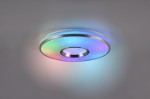 Plafon Realta z pilotem, wykonany z aluminium, w kształcie okrągłym. Emituje światło RGB z efektami kolorowymi, widoczny centralny otwór. Oświetlenie montowane na suficie, w tle jasna ściana.