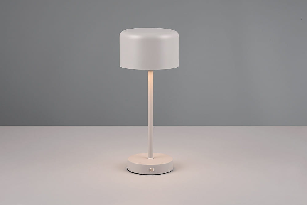 Lampa stołowa Jeff w kolorze szarym, z okrągłą podstawą i cylindrycznym kloszem. Ujęcie frontalne, lampa stoi na płaskiej powierzchni. Widoczny przycisk na podstawie do włączania. Źródło światła LED o mocy 1,5W.