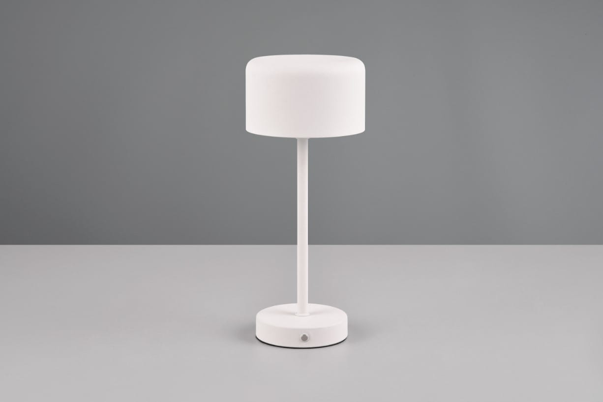 Lampa stołowa Jeff w kolorze białym, z cylindrycznym kloszem na cienkiej, prostej nodze i okrągłej podstawie. Widoczny przycisk zasilania na podstawie. Ujęcie frontalne na jednolitym tle.