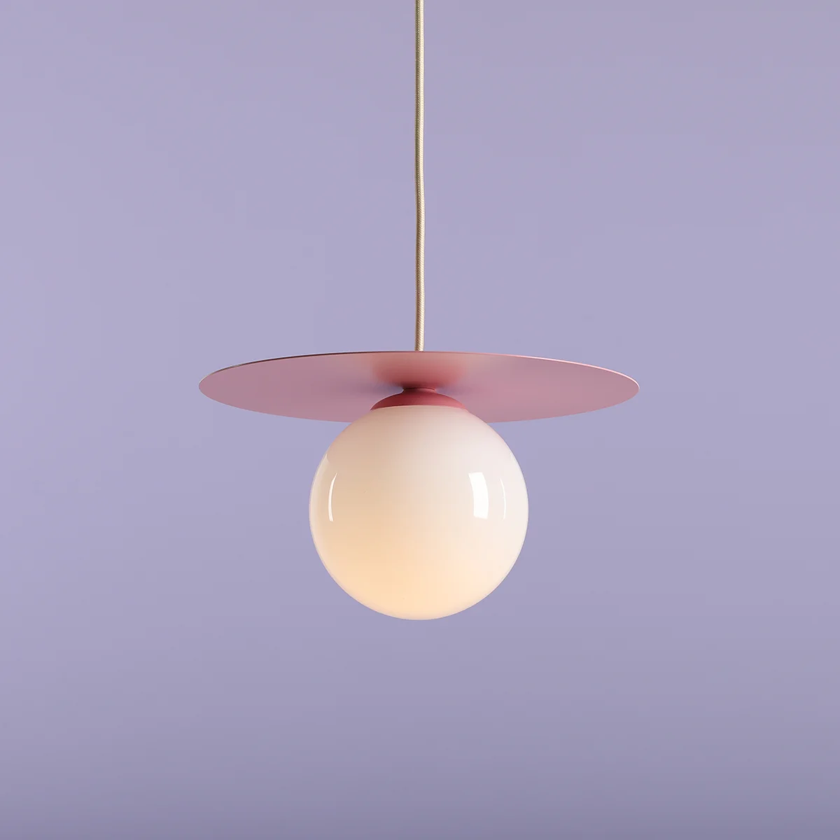 Lampa wisząca Loop Baby Pink S, z okrągłą, matową, białą kulą oraz różową, płaską podstawą. Ujęcie frontalne, zawieszona na cienkim kablu. Tło w delikatnym, jasnym odcieniu fioletu, co podkreśla kolor lampy.