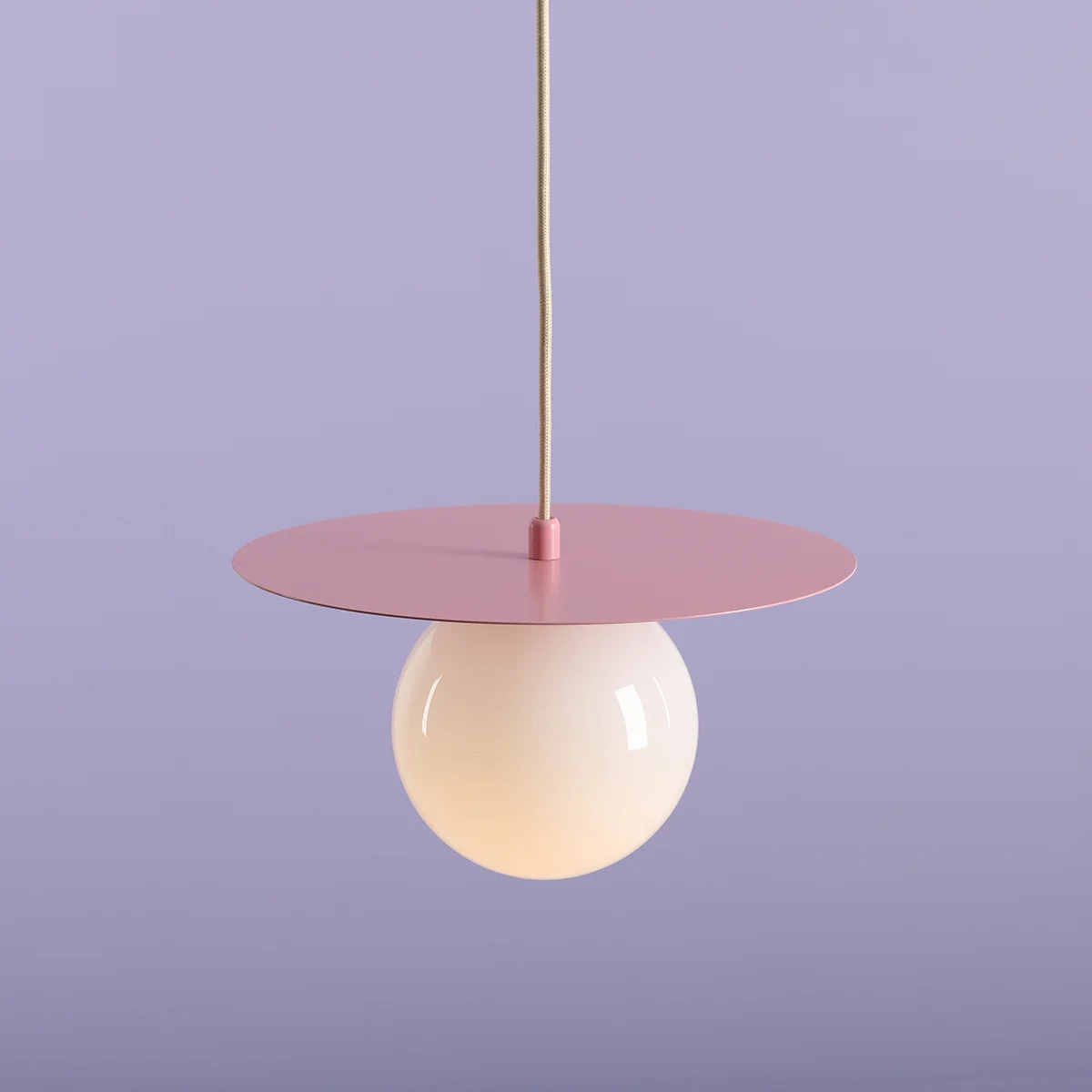 Lampa wisząca Loop Baby Pink S z metalowym, różowym okrągłym kloszem i białą, szklaną kulą. Produkt zawieszony na cienkim przewodzie, z widocznym mocowaniem. Tło w kolorze lawendowym, co podkreśla subtelność designu.