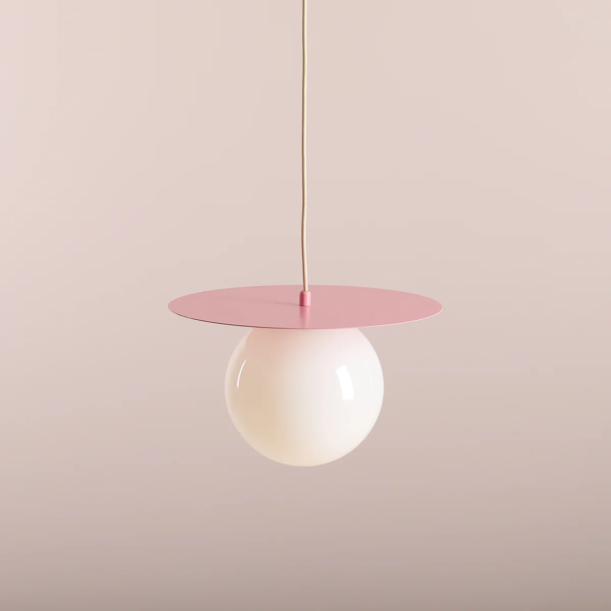 Lampa wisząca Loop Baby Pink M z jednym gniazdem E27. Posiada okrągłą, białą szklaną kulę oraz różową, metalową podstawę w formie talerza. Zawieszona na jasnym przewodzie, prezentuje nowoczesny design na jednolitym tle.