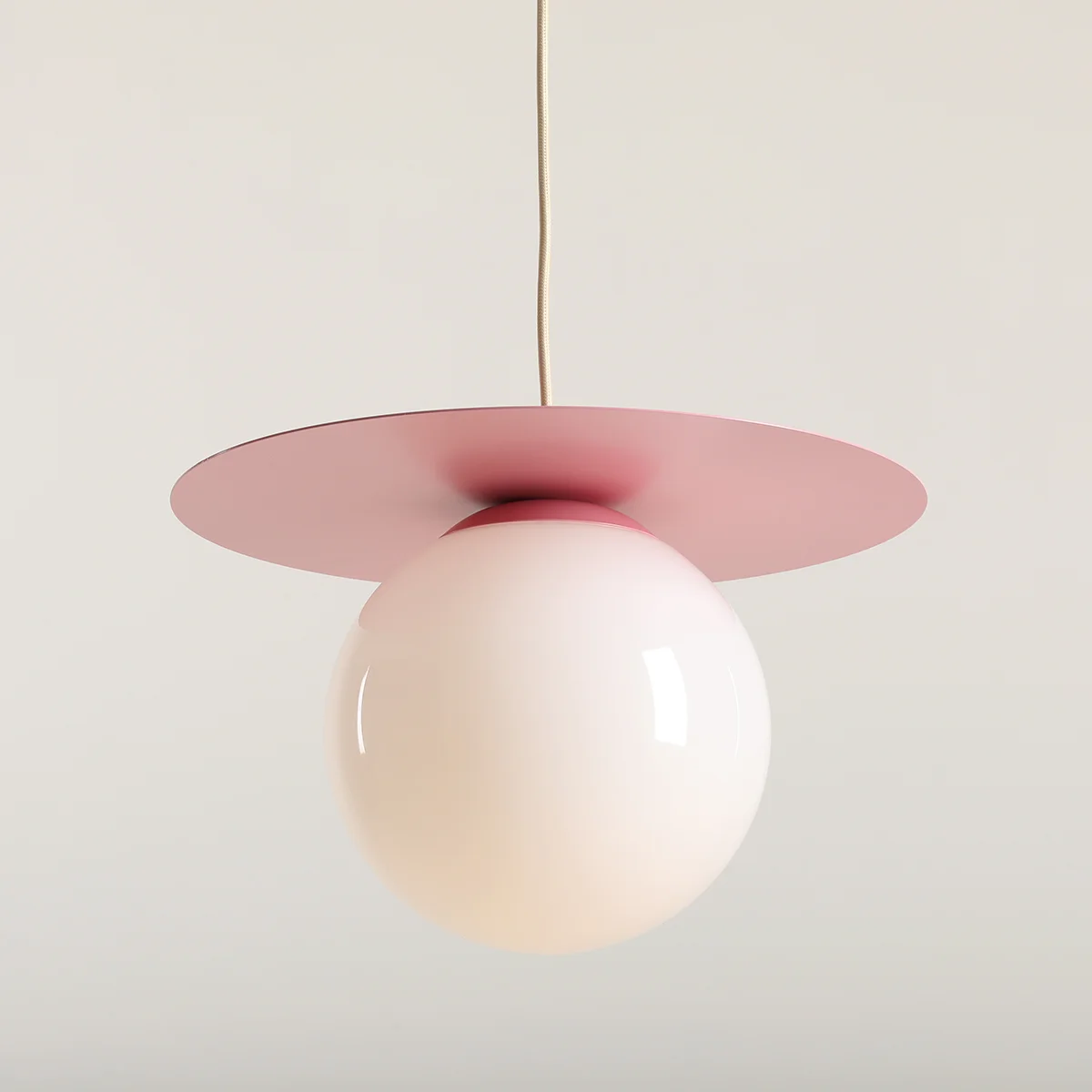 Lampa wisząca Loop Baby Pink M z kloszem w kształcie kuli w odcieniu jasnego różu, umieszczona na okrągłej podstawie w tym samym kolorze. Produkt zawiera miejsce na żarówkę E27, zawieszony na cienkim przewodzie. Tło jasne, jednolite.
