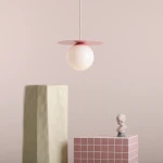 Lampa wisząca Loop Baby Pink M z kulistym kloszem w kolorze białym i różowym metalowym daszkiem. Zawieszona na cienkim przewodzie, w otoczeniu geometrycznych dekoracji w pastelowych odcieniach. Idealna do nowoczesnych wnętrz.