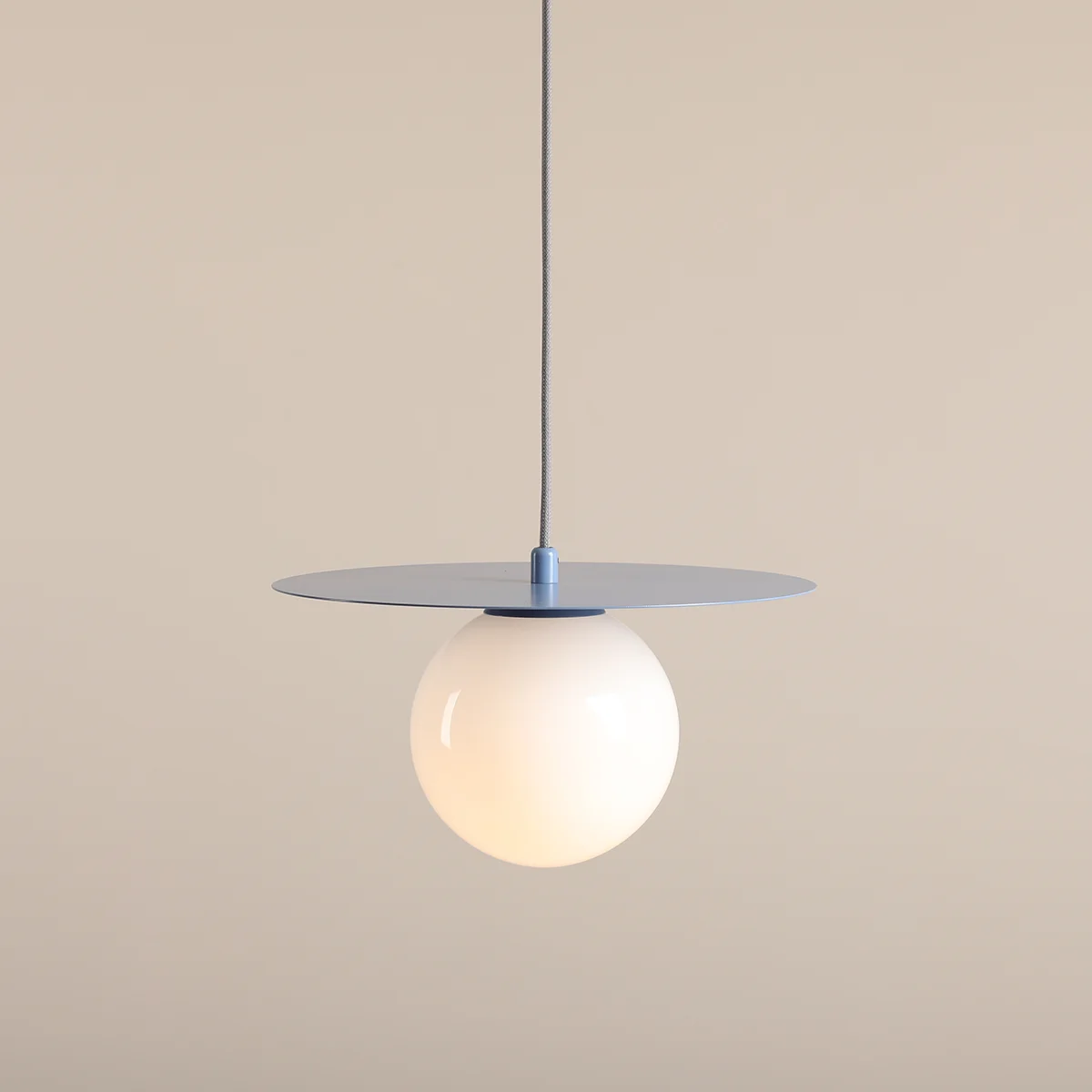 Lampa wisząca Loop w kolorze błękitnym, z okrągłą, białą kulą na metalowej podstawie. Zawieszona na cienkim przewodzie, z płaskim, okrągłym elemencie u góry. Prosta forma, idealna do nowoczesnych wnętrz.