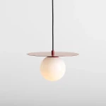 Lampa wisząca Loop Red Wine S z jednym źródłem światła E14. Posiada okrągłą, białą kulę i okrągłą, czerwoną osłonę na górze. Wisi na czarnym kablu, na jasnym tle.