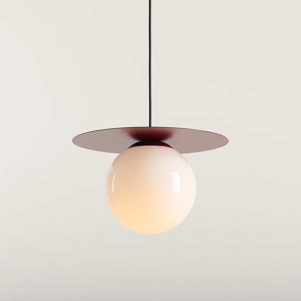 Lampa wisząca Loop Red Wine M z kloszem w kształcie półprzezroczystej kuli w odcieniu białym, zawieszona na czarnym przewodzie. Posiada okrągłą, czerwoną osłonę u góry, nadającą nowoczesny styl. Idealna do różnych wnętrz.