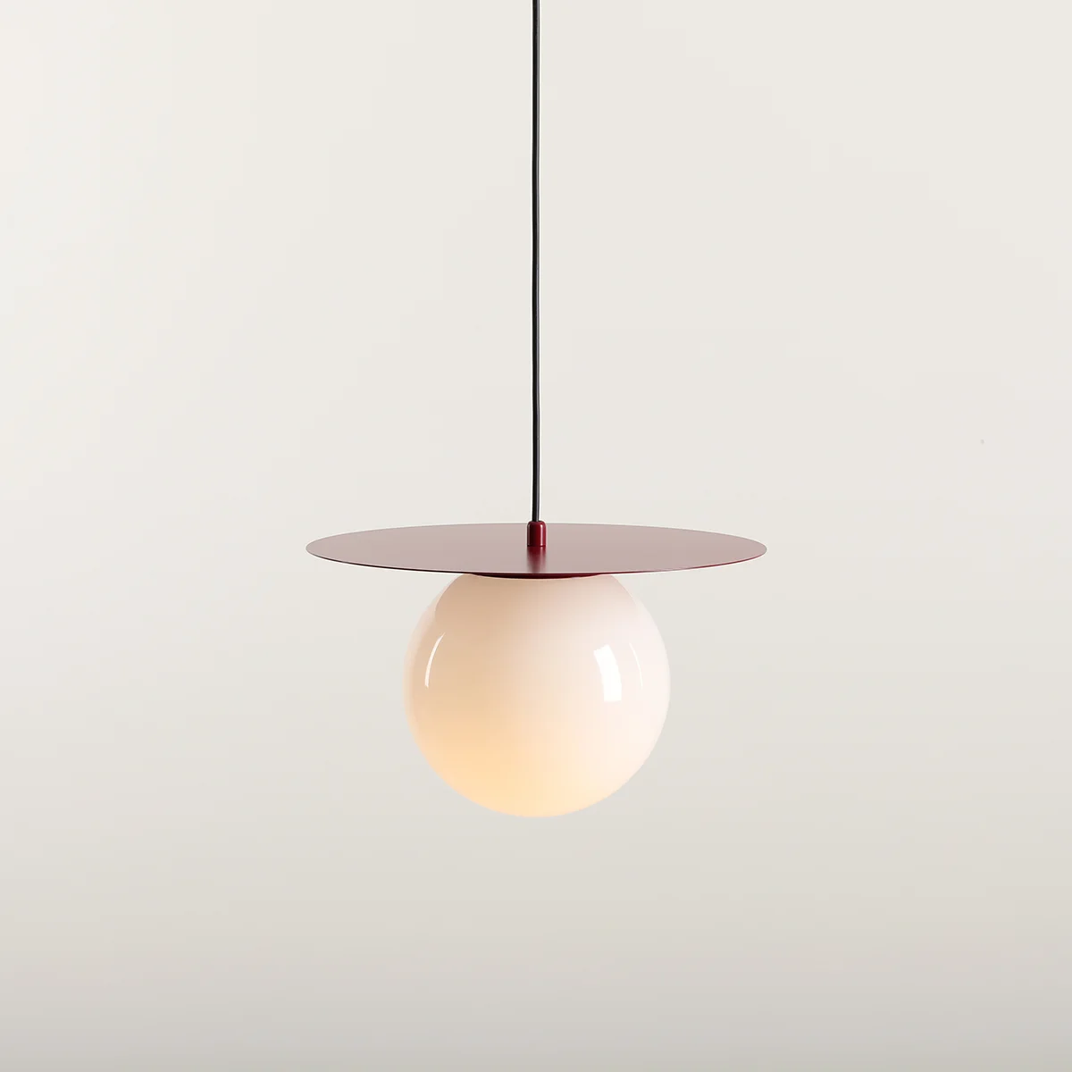 Lampa wisząca Loop Red Wine M z kloszem w kształcie kuli w kolorze mlecznym, zawieszona na czarnym przewodzie, z okrągłą podstawą w odcieniu czerwieni burgundowej. Produkt prezentowany na jasnym tle.
