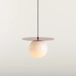 Lampa wisząca Loop Red Wine M z kloszem w kształcie kuli w kolorze mlecznym, zawieszona na czarnym przewodzie, z okrągłą podstawą w odcieniu czerwieni burgundowej. Produkt prezentowany na jasnym tle.