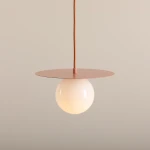 Lampa wisząca Loop Coral S z metalowym, różowym kloszem w kształcie talerza i opalową kulą. Uchwyt z brązowego przewodu. Produkt zawieszony w pozycji pionowej na jednolitym tle.