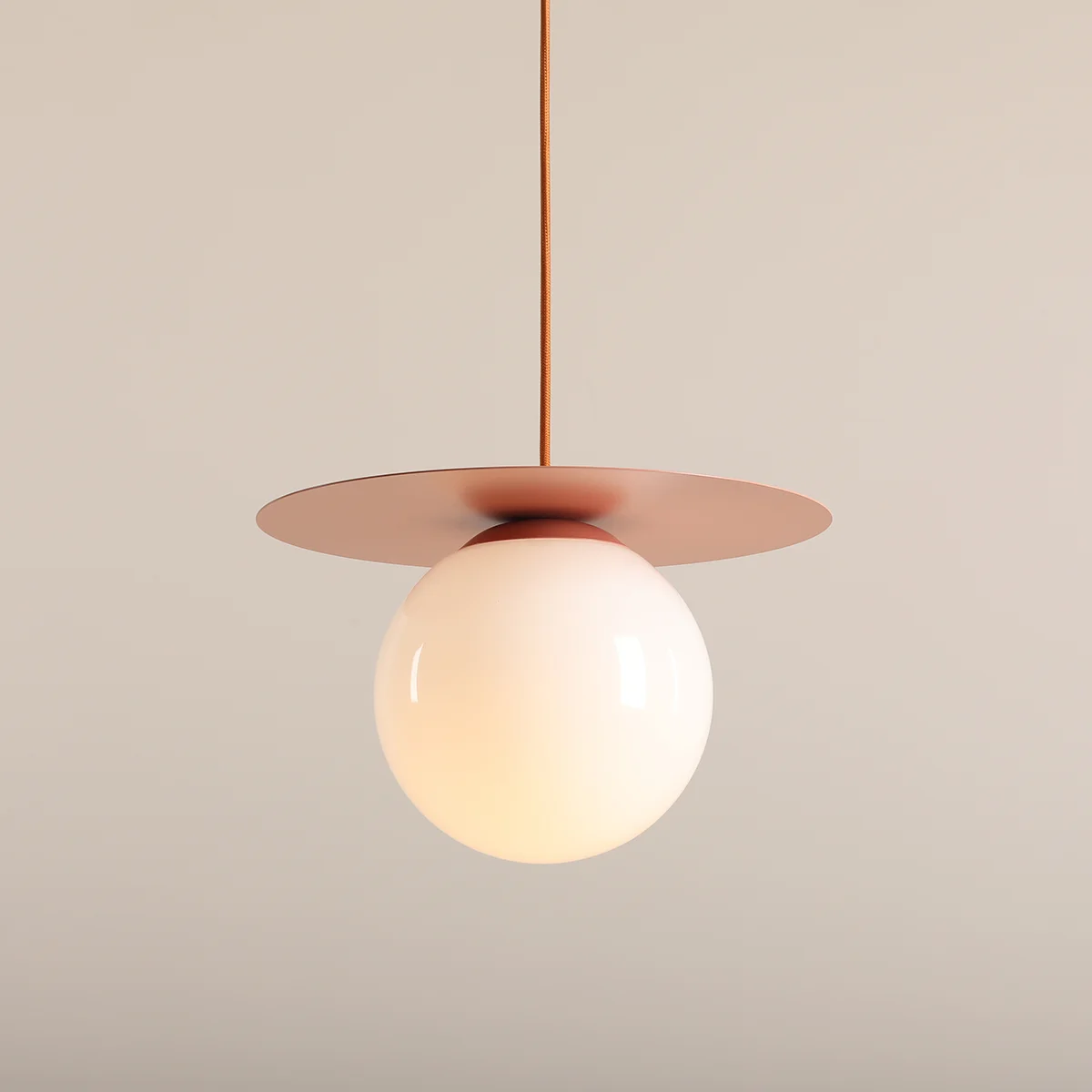 Lampa wisząca Loop Coral M z okrągłym, mlecznym kloszem i płaską, różową podstawą. Zawieszona na kolorowym kablu, w stylu nowoczesnym. Idealna do różnych aranżacji wnętrz. Tło w neutralnym odcieniu.