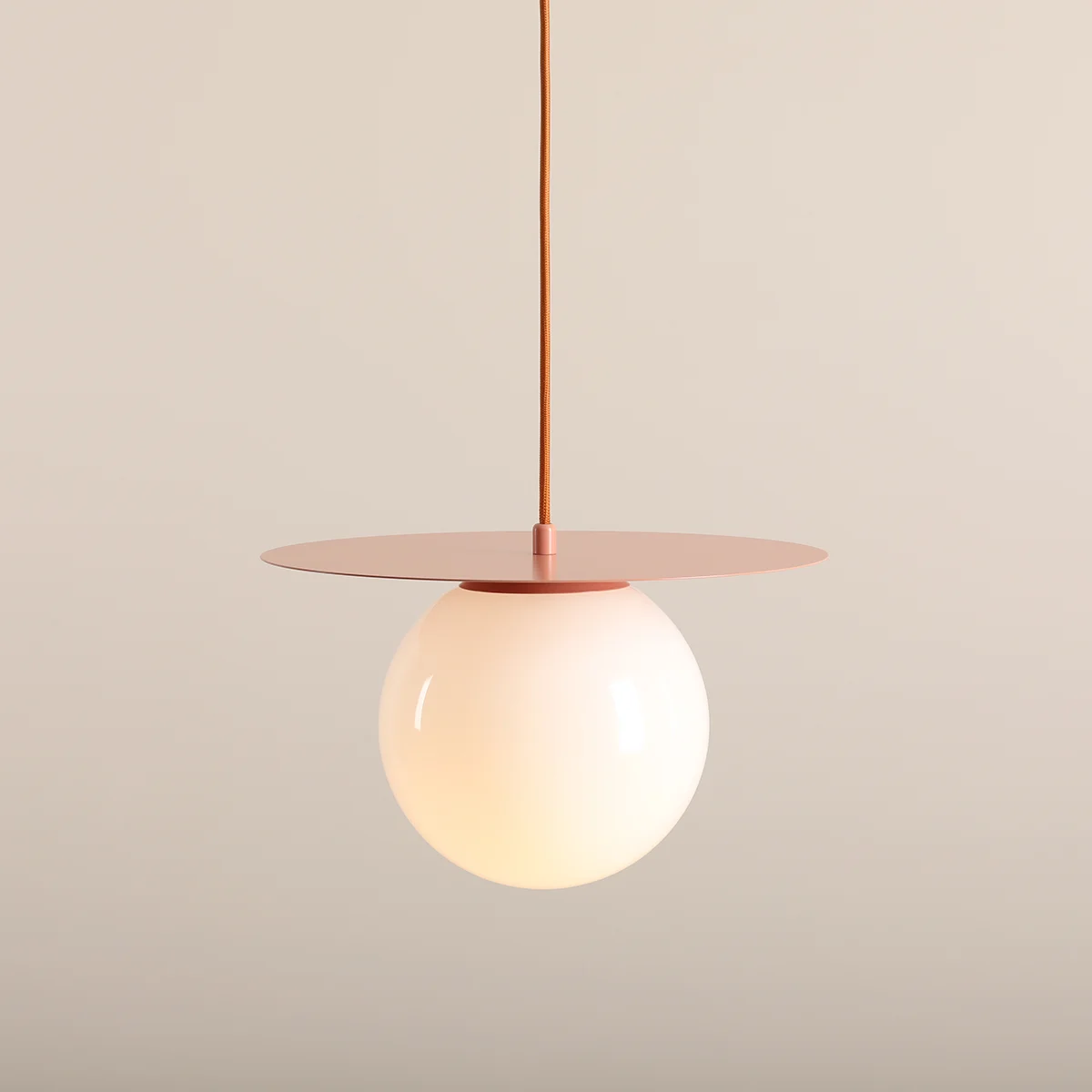 Lampa wisząca Loop Coral M z pojedynczym źródłem światła E27. Kulisty klosz w kolorze mlecznym, zawieszony na cienkim przewodzie, z okrągłą, metalową osłoną w kolorze koralowym. Minimalistyczny design, zawieszona w centralnej pozycji.