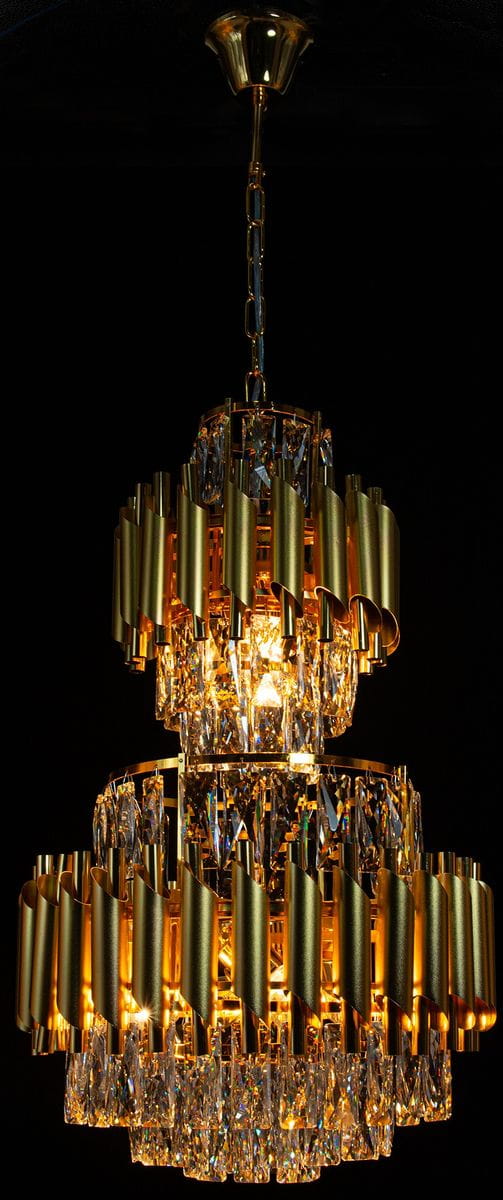Lampa wisząca Wersal 6xE27 w kolorze złotym, z kryształowymi detalami. Posiada dwa poziomy ozdobnych, falistych elementów oraz widoczne źródła światła. Zawieszona na łańcuchu, prezentuje elegancki design w ciemnym tle.