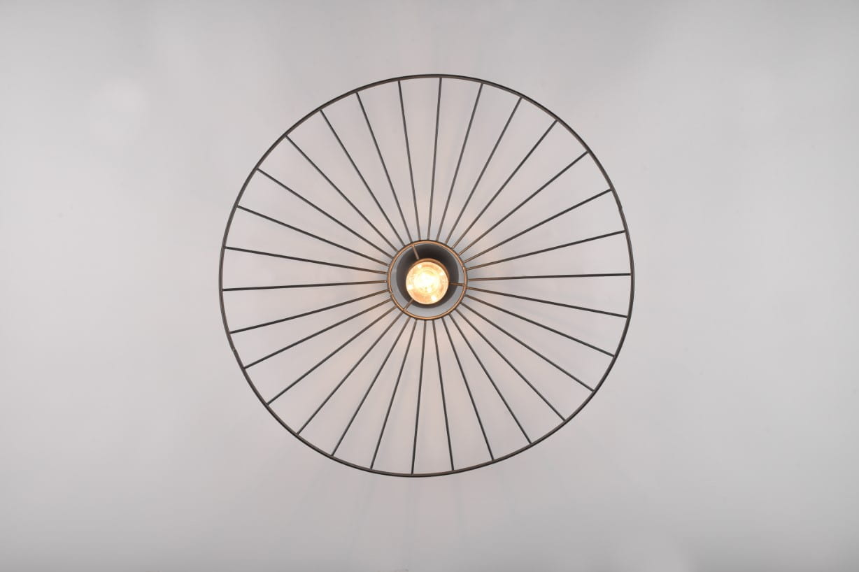 Lampa sufitowa Chapeau w kolorze czarnym z oprawą na jedną żarówkę E27. Widok z dołu, pokazujący okrągłą konstrukcję z metalowych prętów, tworzących promieniście rozchodzący się wzór. Centralnie umieszczona żarówka emituje światło.