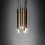 Lampa wisząca 7-punktowa w kolorach mosiężnym, złotym i brązowym, z prostymi, cylindrycznymi kloszami. Ujęcie z dołu, prezentujące lampę zawieszoną na czarnych przewodach. Źródła światła emitują delikatne blaski. Tło w odcieniu szarości.