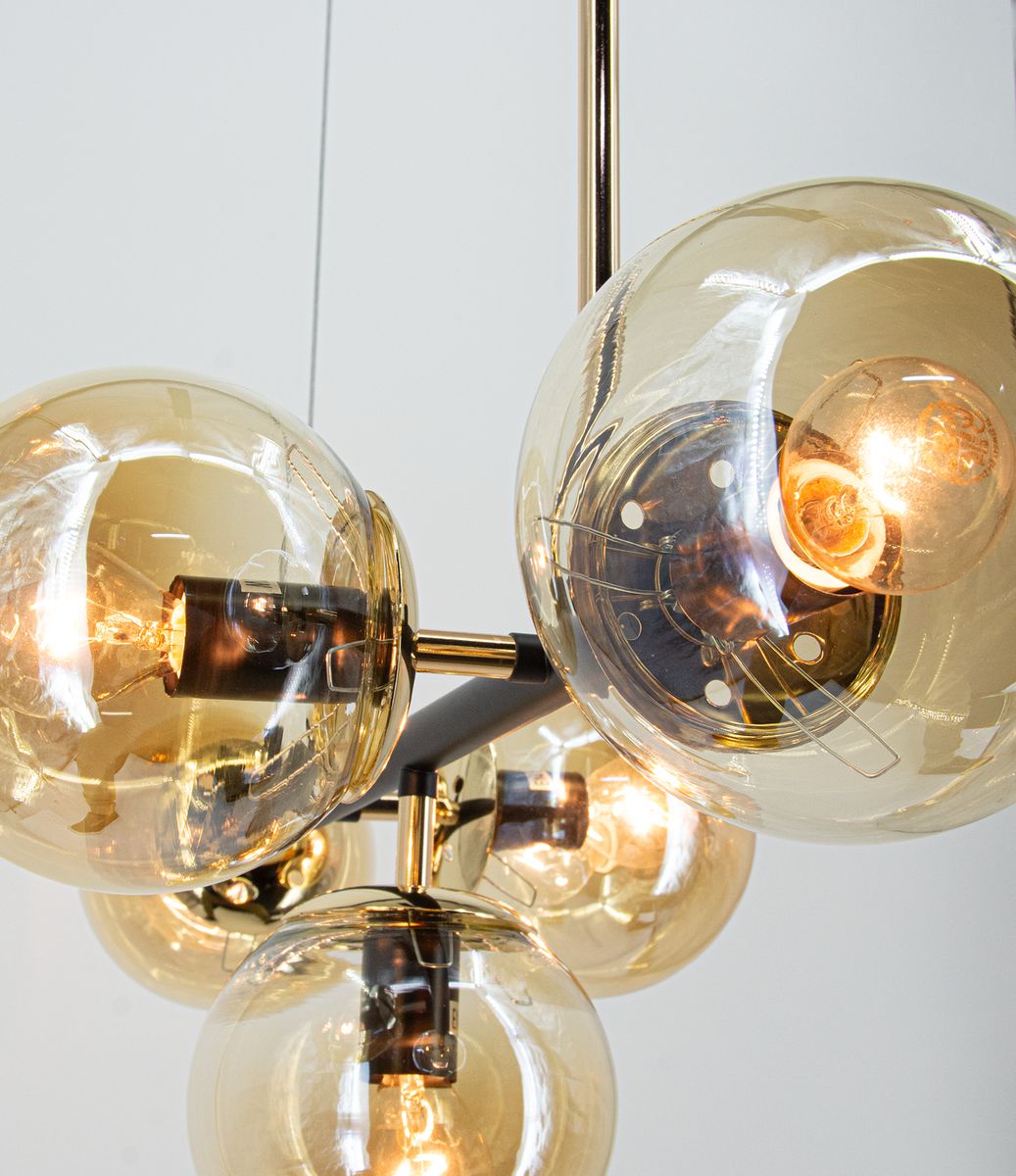Lampa wisząca Greta z pięcioma oprawami E14, w kolorze czarnym i złotym. Posiada szklane klosze w kształcie kul, lekko przyciemnione, które eksponują żarówki, tworząc elegancki efekt świetlny. Ujęcie z góry, z bliska, ukazuje detale konstrukcji.