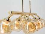 Lampa wisząca Piran 6xE27 w kolorze złotym. Posiada sześć kulistych kloszy z przezroczystego szkła, zawieszonych na metalowej konstrukcji. Klosze mają widoczne źródła światła i są zamocowane pod kątem, co podkreśla nowoczesny design.