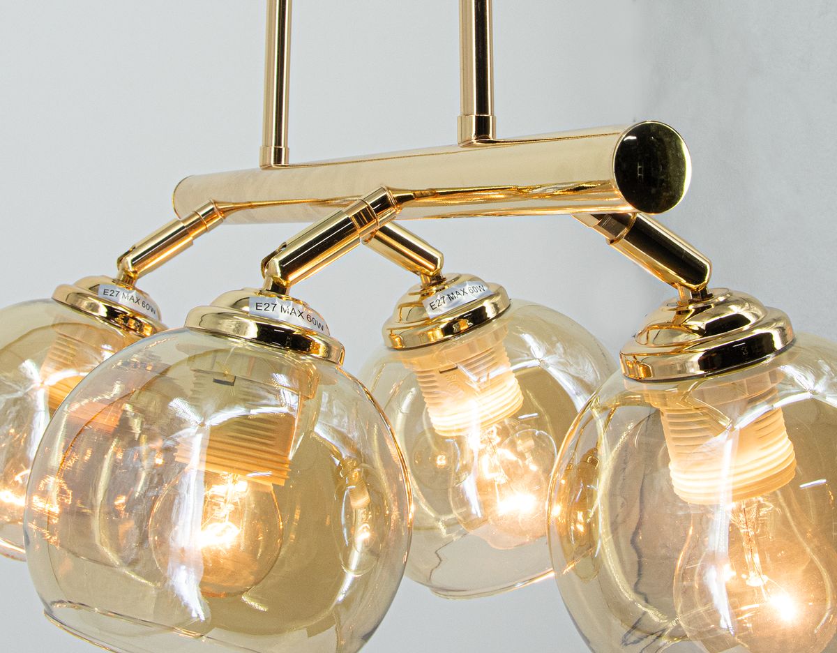 Lampa wisząca Piran 4xE27 w złotym wykończeniu. Cztery szklane klosze w kształcie kul, z widocznymi żarówkami, zawieszone na metalowej konstrukcji. Klosze mają delikatną, przezroczystą fakturę, wiszą w równych odstępach.