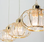 Lampa wisząca Acri 3xE27 w kolorze złotym z przezroczystymi kloszami. Klosze mają metalową ramę i dekoracyjne szczotkowane wykończenie. Ujęcie z przodu, prezentujące trzy źródła światła, zawieszone na cienkich przewodach.