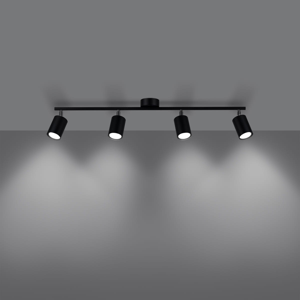 Czarna lampa sufitowa Lemmi z czterema reflektorami GU10, zamontowana na prostokątnej podstawie. Reflektory skierowane są w dół, emitując światło na szarym tle. Minimalistyczny design, idealna do nowoczesnych wnętrz.