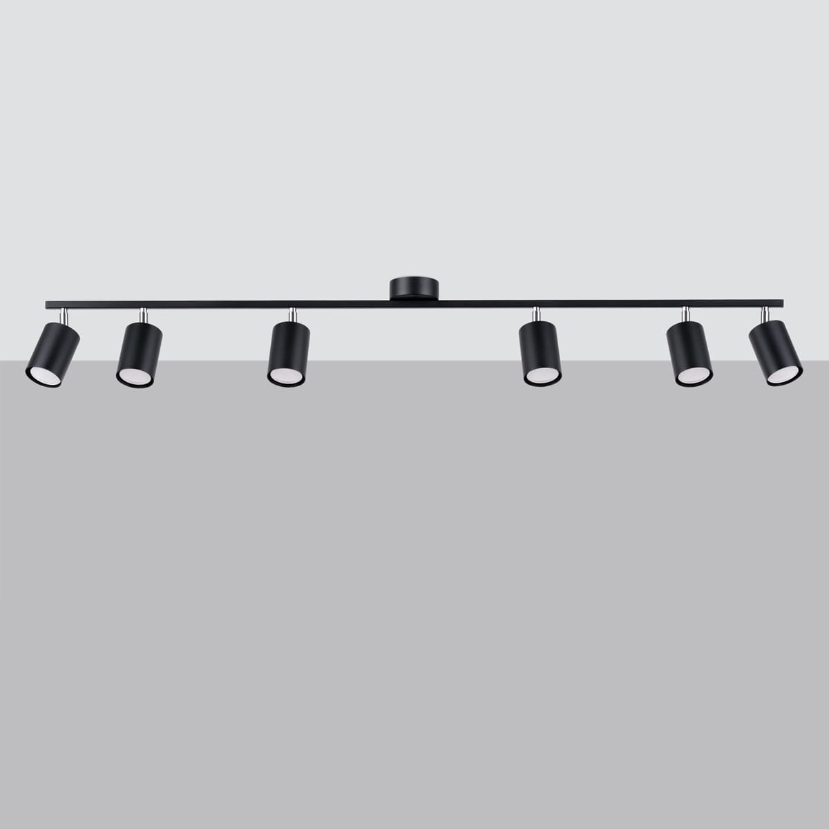 Lemmi lampa sufitowa (spot) z sześcioma oprawami na żarówki GU10 w kolorze czarnym. Ułożona poziomo, z cylindrycznymi kloszami, zamocowana na prostokątnej listwie. Tło jasnoszare, co podkreśla elegancki design lampy.