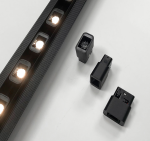 Soczewka LED do szyny magnetycznej 2W/3000K w kolorze czarnym, prostokątna, z widocznymi złączami i elementami montażowymi, umieszczona obok szyny z diodami LED. Tło zdjęcia jasne, co podkreśla charakterystyki produktu.
