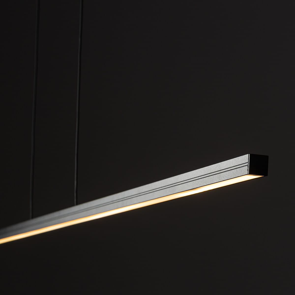Czarna lampa wisząca Bar L150 z jedną diodą LED o mocy 24W i barwie światła 3000K. Produkt ma prostokątny kształt, zawieszony na cienkich przewodach, z widocznym źródłem światła na dolnej krawędzi. Tło ciemne, minimalistyczne.