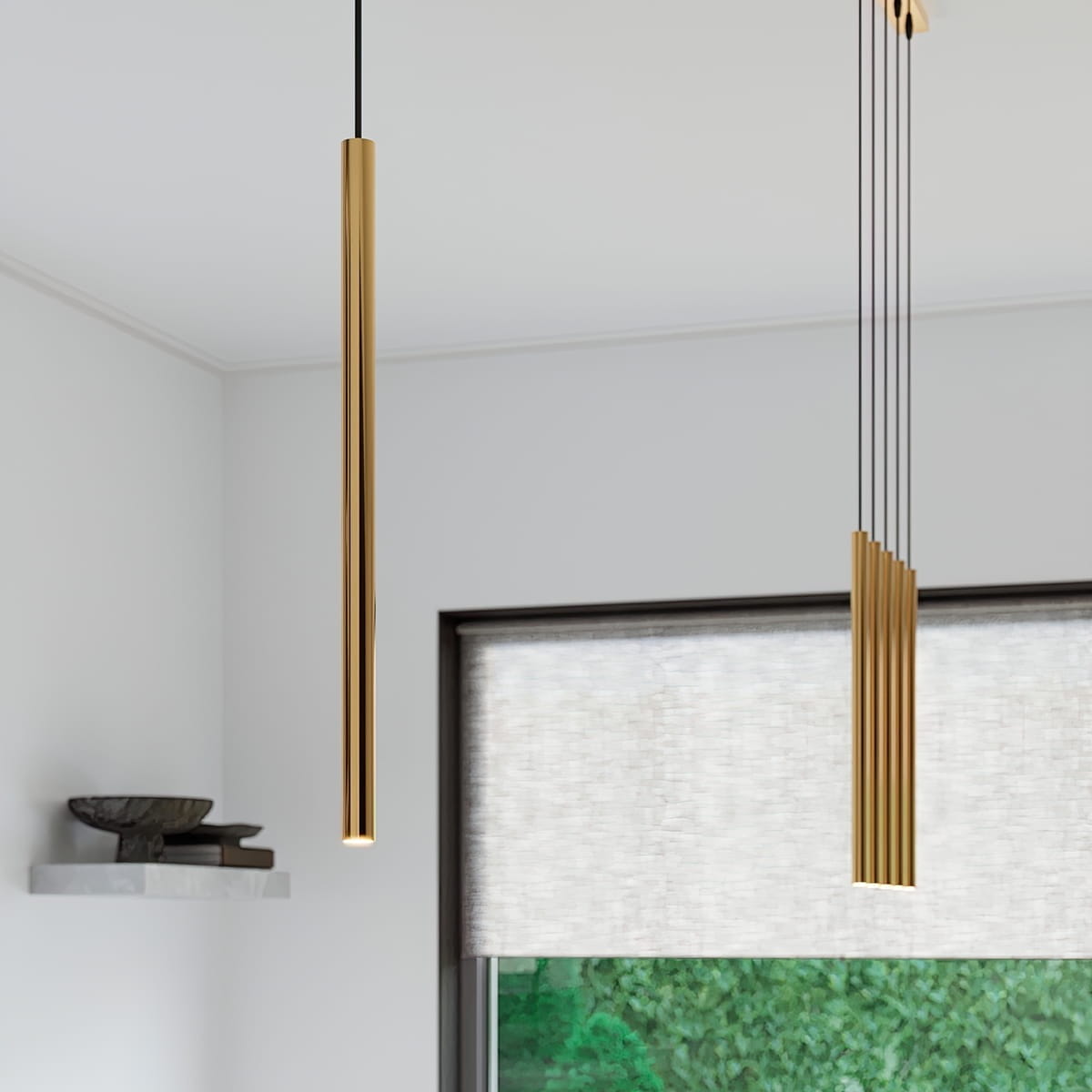 Lampa wisząca Pastelo 5xG9 w kolorze złotym, składająca się z prostych, cylindrycznych elementów. Zawieszona na cienkich linkach, w nowoczesnym wnętrzu z oknem i roletą. W tle widoczna półka z dekoracjami.