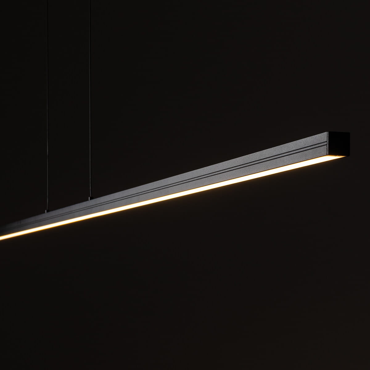 Lampa wisząca Bar L180 w kolorze czarnym, z prostokątnym, smukłym korpusem. Wyposażona w diodę LED o mocy 27W, emitującą ciepłe światło (3000K). Zawieszona za pomocą cienkich linki, z widocznym podświetleniem na krawędzi.