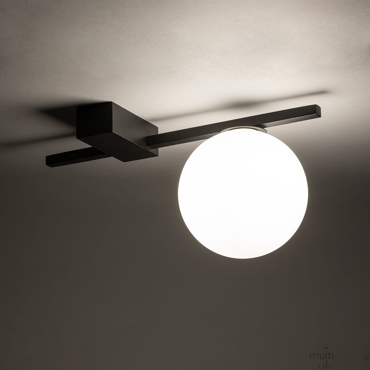 Lampa sufitowa Pik z jednym gniazdem G9, w kolorze czarnym. Zamontowana na suficie, z prostokątną podstawą oraz okrągłym, mlecznym kloszem, emitującym miękkie światło. Kąt ujęcia z góry, na jednolitym tle.