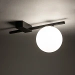Lampa sufitowa Pik z jednym gniazdem G9, w kolorze czarnym. Zamontowana na suficie, z prostokątną podstawą oraz okrągłym, mlecznym kloszem, emitującym miękkie światło. Kąt ujęcia z góry, na jednolitym tle.