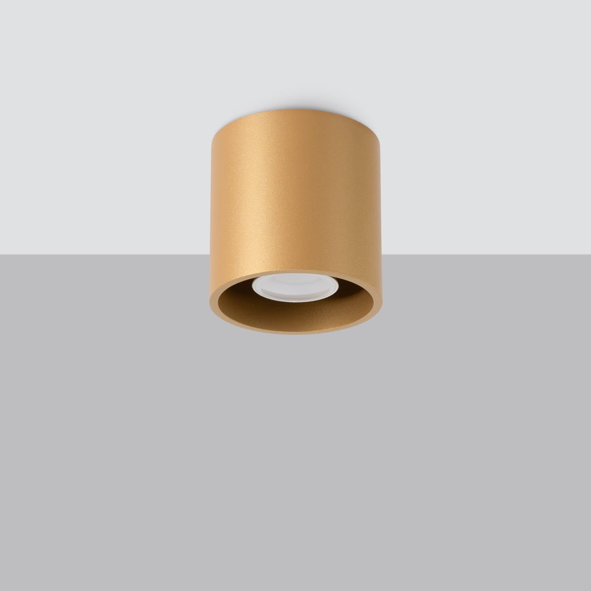 Lampa sufitowa Orbis w kolorze złotym, o cylindrycznym kształcie, z miejscem na żarówkę GU10, montowana na suficie. Widok z dołu na gładką, matową powierzchnię. Tło w odcieniu szarym.