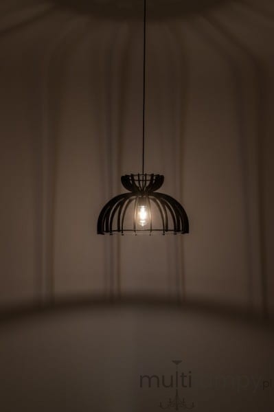 Czarna lampa wisząca Kymi C z kloszem w formie ażurowej konstrukcji, umieszczona w centralnej części na cienkim przewodzie. Widoczna żarówka E27, rzucająca cień na ścianę. Lampa wisi w prostym otoczeniu na jednolitym tle.
