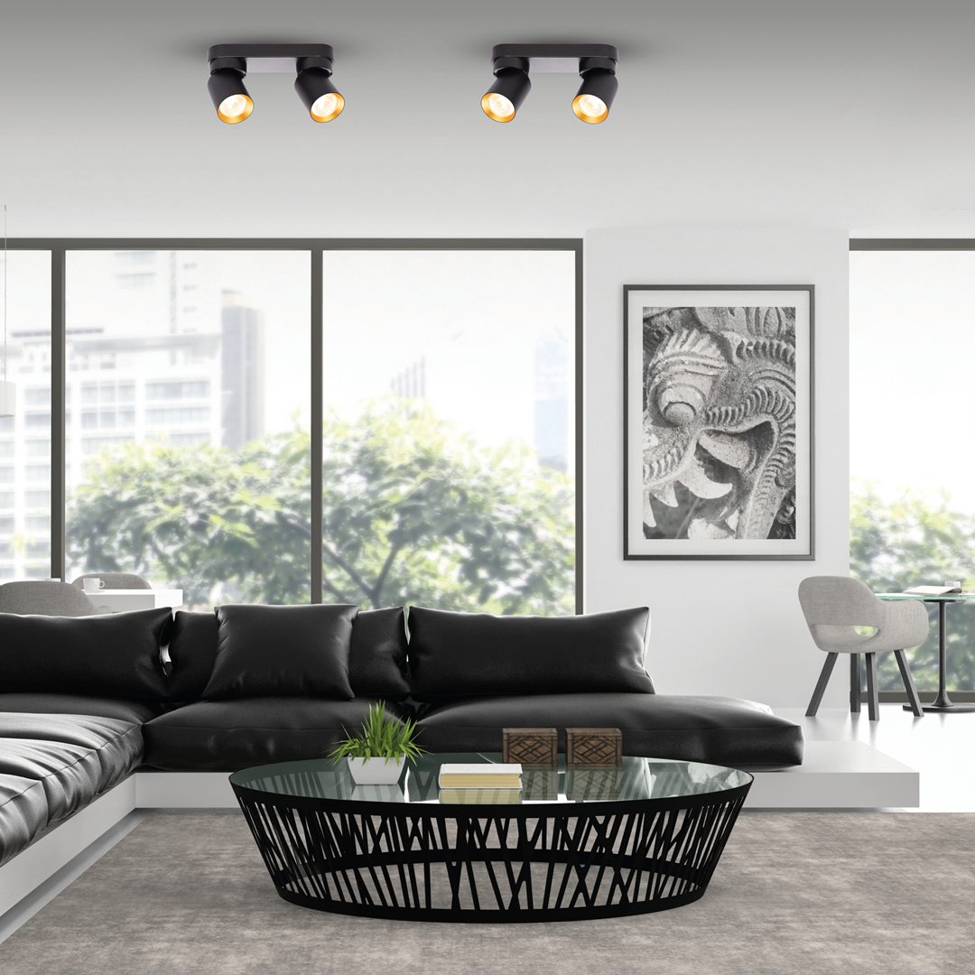 Czarna lampa sufitowa Andy z dwoma reflektorami GU10, umieszczona na białym stelażu. Reflektory mają złote wnętrza, co nadaje elegancki wygląd. Produkt montowany na suficie, w nowoczesnym wnętrzu z sofą, stolikiem kawowym i dużymi oknami.