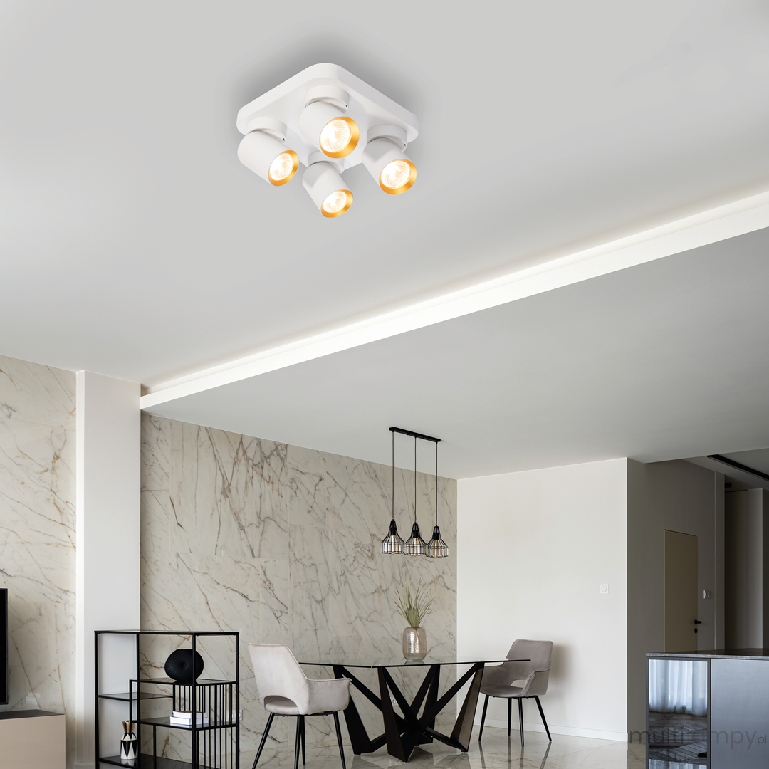 Lampa sufitowa Andy z czterema reflektorami GU10 w kolorze białym i złotym, zamontowana na suficie, w nowoczesnym wnętrzu z marmurową ścianą i eleganckim stołem. Reflektory skierowane w różne strony, zapewniające oświetlenie przestrzeni.