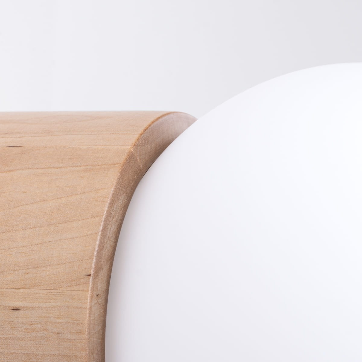 Kinkiet Boomo 1xG9 z naturalnego drewna, z zaokrąglonym krawędzią i białym kloszem. Ujęcie z bliska na detal drewna i klosza, podkreślające fakturę i łączenie materiałów. Tło jasne, minimalistyczne.