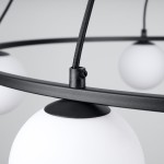 Lampa wisząca Yoli 5xG9 w kolorze czarnym, z metalowym pierścieniem i pięcioma białymi, okrągłymi kloszami. Widoczny detal łączenia kabla z oprawą. Produkt zwisający, w zbliżeniu na elementy konstrukcyjne.