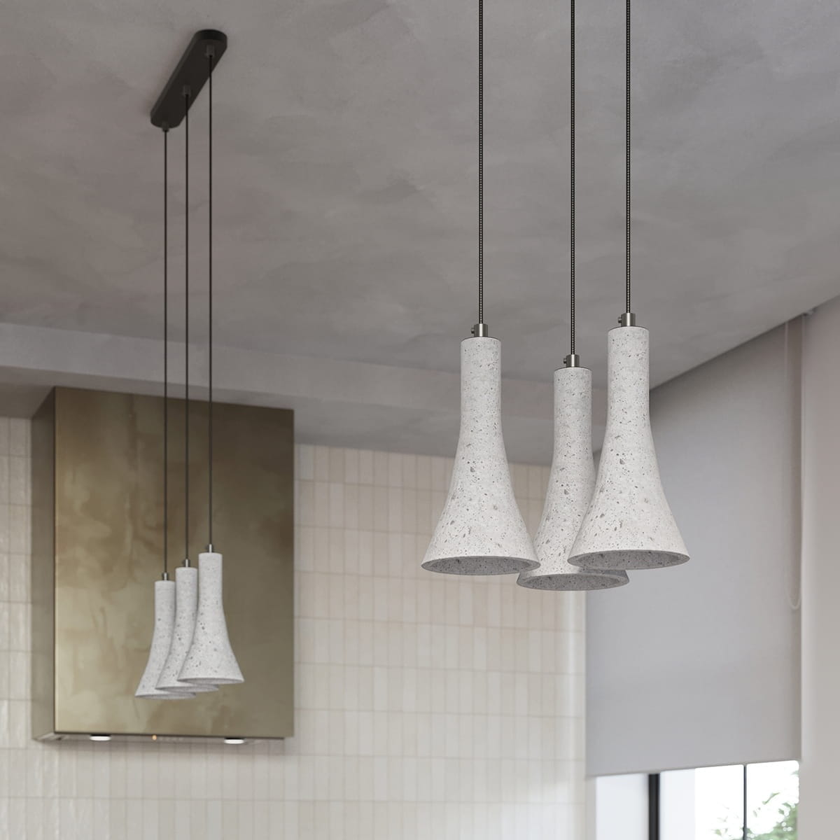 Lampa wisząca Rea z trzema kloszami w kształcie dzwonu, wykonana z betonu w odcieniu jasnoszarym. Zawieszona na cienkich, czarnych linkach, montowana do sufitu. Oświetlenie idealne do nowoczesnych wnętrz, wykończone metalowymi detalami.