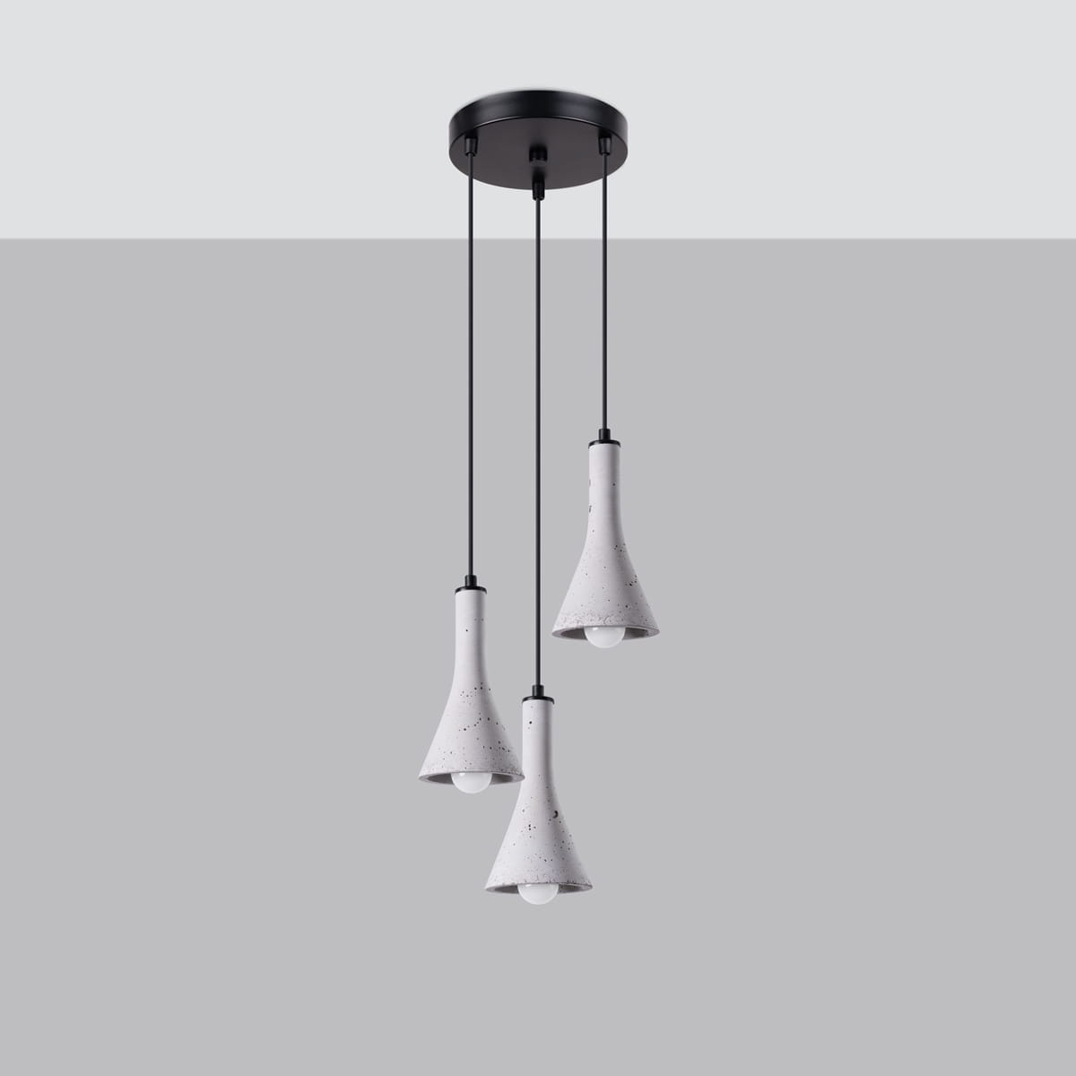 Lampa wisząca Rea z trzema kloszami w kształcie dzwonów wykonanymi z betonu w kolorze szarym, zawieszona na czarnych linkach. Utrzymana w nowoczesnym stylu, z montażem sufitowym. W tle jednolite szare tło.