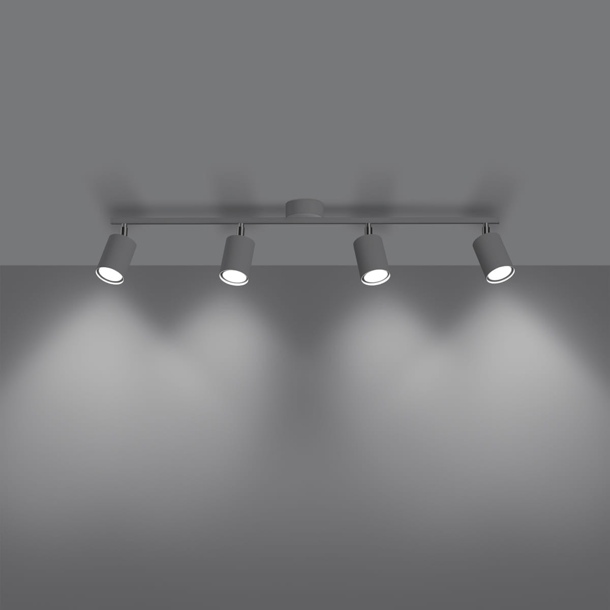 Lemmi lampa sufitowa (spot) z czterema oprawami GU10 w białym kolorze, zamontowana na metalowym stelażu. Ujęcie z dołu, z widocznym oświetleniem skierowanym na ścianę, na szarym tle.