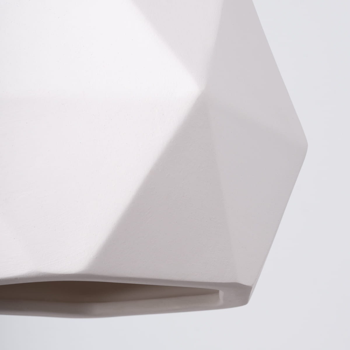 Biała lampa wisząca Mint z kloszem w kształcie diamentu. Materiał matowy, z widocznymi, geometrycznymi krawędziami. Zainstalowane mocowanie na żarówkę E27. Ujęcie z bliska, ukazujące szczegóły faktury i kształtu.